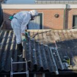professional asbestos removal. men in protective suits are removing asbestos cement corrugated roofing
